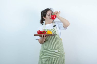 Önlüklü genç bir kız elinde taze sebzelerle tahta bir tahta tutuyor. Yüksek kalite fotoğraf