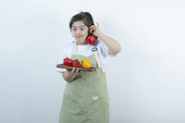 Önlüklü genç bir kız elinde taze sebzelerle tahta bir tahta tutuyor. Yüksek kalite fotoğraf