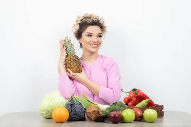 Genç bayan model ananas elinde, masada meyve dolu oturuyor. Yüksek kalite fotoğraf
