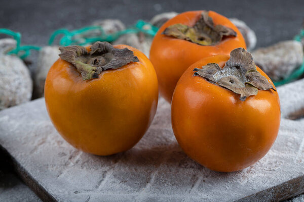 Dried persimmons with sugar powder around fresh persimmons on black surface. High quality photo