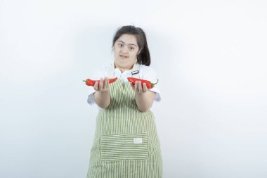 Kareli önlüğün içinde duran ve elinde iki kırmızı acı biber tutan genç ve güzel bir kız. Yüksek kalite fotoğraf