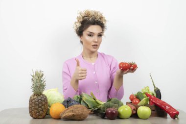Masada oturan ve elinde taze kırmızı domateslerle güzel bir kadın. Yüksek kalite fotoğraf