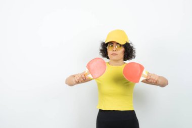 Beyaz arka planda tenis raketleriyle poz veren genç bir kadın 