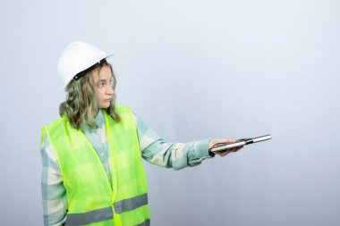 Genç bayan mühendisin beyaz duvardan defter dağıtırken çekilmiş bir fotoğrafı. Yüksek kalite fotoğraf