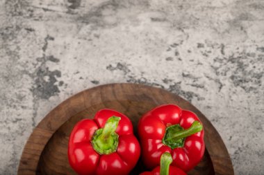Wooden plate of ripe red bell peppers for healthy eating on stone surface. High quality photo