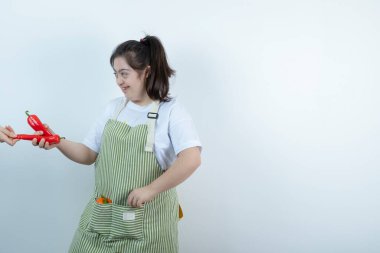 Önlüklü genç bir kız beyaz duvara kırmızı kırmızı biber veriyor. Yüksek kalite fotoğraf