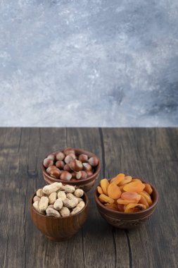 Tahta masada kurutulmuş kayısı meyveleri ve sağlıklı fındıklarla dolu tahta kaseler. Yüksek kalite fotoğraf