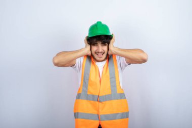 Kulaklarını tutan yeşil şapkalı genç bir inşaat işçisi. Yüksek kalite fotoğraf