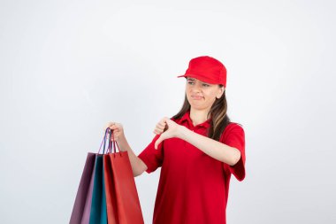 Kırmızı üniformalı genç bir kızın başparmağını göstermesi ve alışveriş torbaları tutması. Yüksek kalite fotoğraf