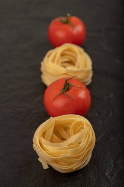 Çiğ tagliatelle yuvaları ve siyah yüzeyde taze domatesler. Yüksek kalite fotoğraf