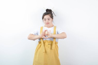 Genç ve güzel kız model ayakta duruyor ve elleri beyaz duvara dayalı kalp sembolü yapıyor. Yüksek kalite fotoğraf