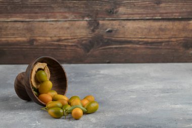 Mermer zemin üzerinde yaprakları olan sarı taze kumkatlarla dolu ahşap bir tabak. Yüksek kalite fotoğraf