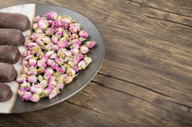 Tahta masanın üzerinde kurumuş gül çiçekleri olan bir tabak çikolata. Yüksek kalite fotoğraf