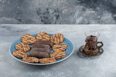 Mavi tabak dolusu çikolatalı kek ve bir bardak sıcak çayla kepekli kurabiye. Yüksek kalite fotoğraf