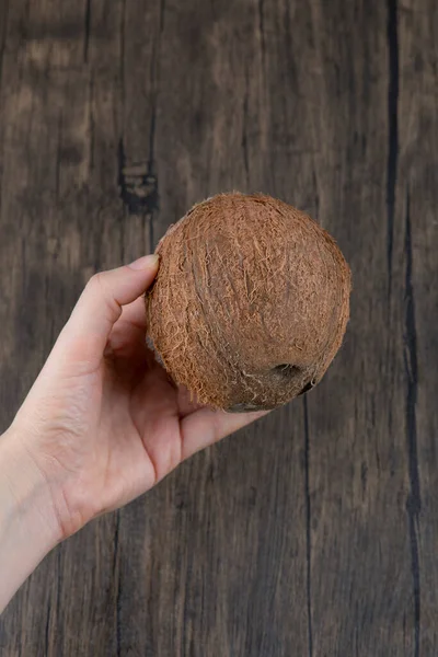 Vrouwelijke Hand Die Rijpe Hele Kokosnoot Een Houten Tafel Houdt — Stockfoto