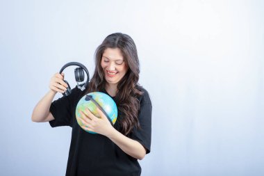 Ayakta duran ve kulaklıkla dünyayı tutan gülümseyen genç bir kadın. Yüksek kalite fotoğraf