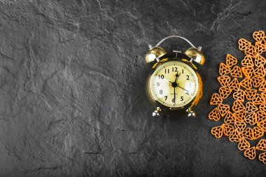 Siyah zemin üzerinde çalar saat olan çiğ makarna yığını. Yüksek kalite fotoğraf