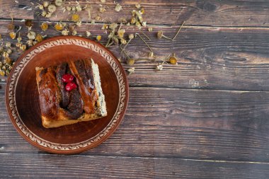 Ahşap bir masaya yerleştirilmiş haşhaş tohumlu kahverengi bir tabak turta ve kurutulmuş çiçekler.