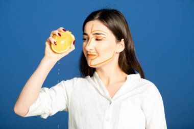 Portakal meyvesinin yarısını tutan yüzü boyalı güzel bir kadının fotoğrafı. Yüksek kalite fotoğraf