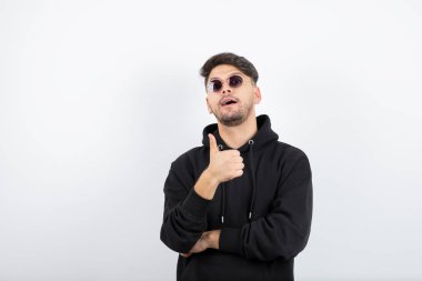 Gözlüklü, genç ve yakışıklı bir adamın ayakta başparmağını kaldırdığı fotoğraf. Yüksek kalite fotoğraf