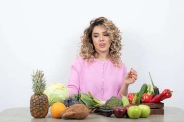 Kıvırcık kadın bir sürü taze sebzeyle masada oturuyor.