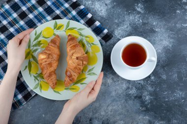 Renkli bir tabak taze kruvasan ve mermer arka planda beyaz bir fincan sıcak çay. Yüksek kalite fotoğraf
