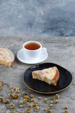 Lezzetli bir parça kek ve beyaz bir fincan sıcak çay ile siyah bir tabak. Yüksek kalite fotoğraf