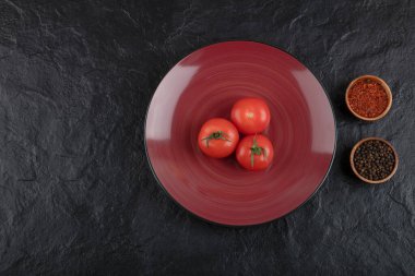 Siyah zemin üzerinde biber ve biber tozu olan üç taze kırmızı domates tabağı. Yüksek kalite fotoğraf