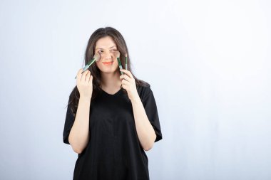 Beyaz arka planda fırçayla makyaj yapan genç ve güzel bir model resmi. Yüksek kalite fotoğraf