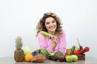 Kıvırcık kadın bir sürü taze sebzeyle masada oturuyor. Yüksek kalite fotoğraf