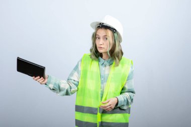 Genç bayan mühendisin beyaz duvardan defter dağıtırken çekilmiş bir fotoğrafı. Yüksek kalite fotoğraf