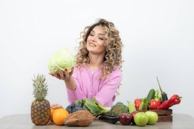 Kıvırcık kadın bir sürü taze sebzeyle masada oturuyor.