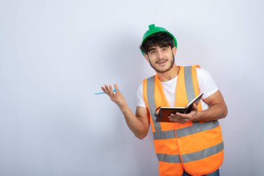 Beyaz duvarın üzerinde duran yeşil şapkalı yakışıklı erkek mühendis. Yüksek kalite fotoğraf