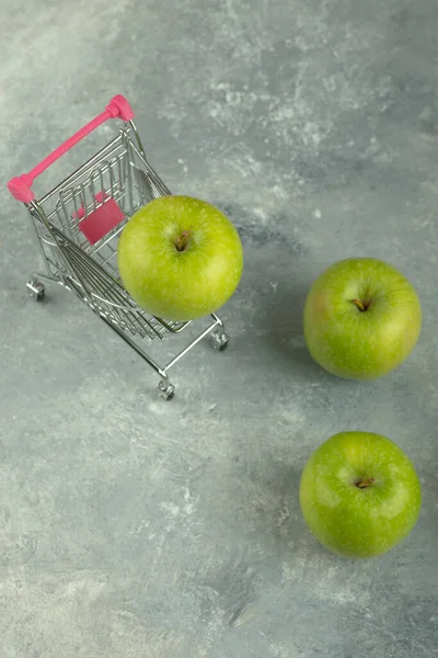 大理石の背景にショッピングカートと緑のジューシーなリンゴ 高品質の写真 — ストック写真