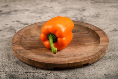 Orange colored sweet bell pepper placed on wooden plate. High quality photo