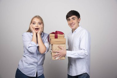 Gülümseyen adam gri arka planda hediyelerle kız arkadaşına sürpriz yapıyor. Yüksek kalite fotoğraf