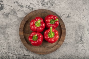 Wooden plate of ripe red bell peppers for healthy eating on stone surface. High quality photo