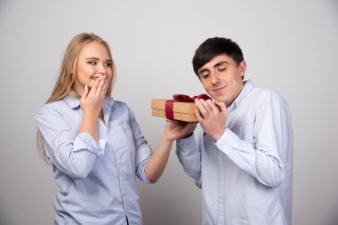 Güzel kız erkek arkadaşına bakıyor ve ona gri arka planda bir hediye veriyor. Yüksek kalite fotoğraf