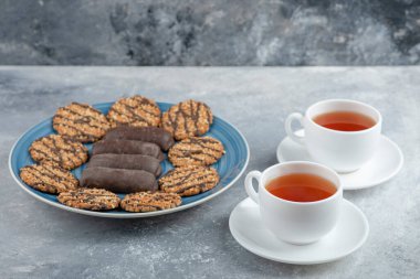 Mavi tabak dolusu çikolatalı kek ve bir fincan sıcak çayla kepekli kurabiye. Yüksek kalite fotoğraf