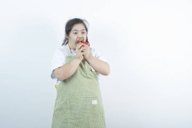 Kareli önlüğün içinde duran ve kırmızı dolma biber yiyen genç ve güzel bir kız. Yüksek kalite fotoğraf