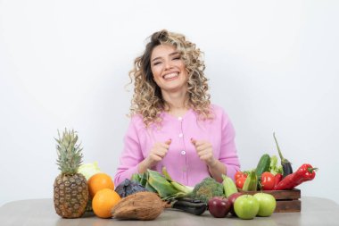 Kıvırcık kadın bir sürü taze sebzeyle masada oturuyor.