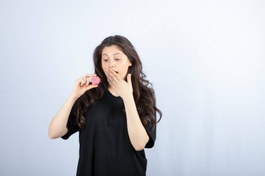 Siyah kıyafetli genç kız beyaz arka planda pembe kurabiye tutuyor. Yüksek kalite fotoğraf