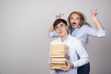Genç ve sevimli bir çift ellerinde kitaplarla gri arka planda kameraya poz veriyorlar. Yüksek kalite fotoğraf