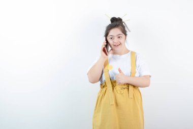 Genç ve güzel kız model ayakta duruyor ve beyaz duvara karşı cep telefonuyla konuşuyor. Yüksek kalite fotoğraf