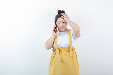 Genç ve güzel kız model ayakta duruyor ve beyaz duvara karşı cep telefonuyla konuşuyor. Yüksek kalite fotoğraf