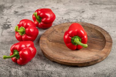 Wooden plate of ripe red bell peppers on stone surface. High quality photo