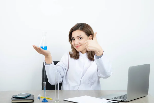 白いコートの少女薬剤師がガラス瓶を持って親指を立てている 高品質の写真 — ストック写真