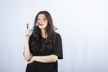 Beyaz arka planda fırçayla makyaj yapan genç modelin portresi. Yüksek kalite fotoğraf