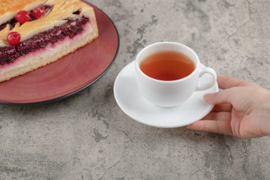 Taş zeminde, lezzetli kekin yanında beyaz bir fincan çay tutan bir kadın. Yüksek kalite fotoğraf