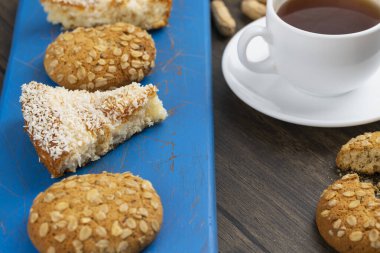 Tahta bir masaya yerleştirilmiş yulaf ezmeli kurabiyeler, bir dilim turta ve bir fincan çay. Yüksek kalite fotoğraf